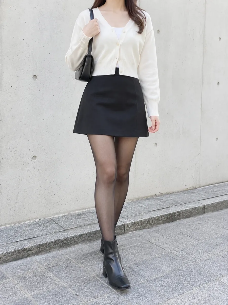 アイボリーのカーディガンに黒のスカートとショートブーツを合わせた女性の服装